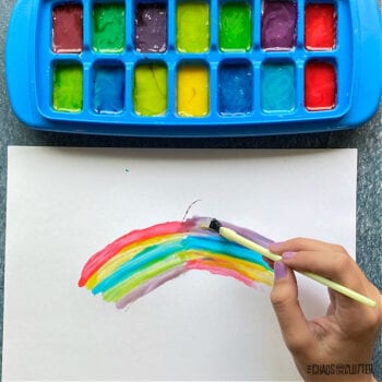 ice cube tray with paint while a hand paints a rainbow with a yellow brush