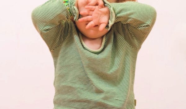 a young girl wearing a green and white striped long sleeve shirt and pink pants sits cross legged on the floor with her hands covering her eyes. The words "How to Stop Sensory Overload from Turning into a Sensory Overload".
