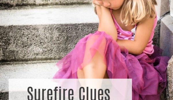 A little girl in a pink princess dress with blonde pigtails and a gold decoration in her hair sits with one leg crossed over the other on a grey outdoor staircase. The words "Surefire Clues Your Child has Sensory Issues" are overlaid on the image.