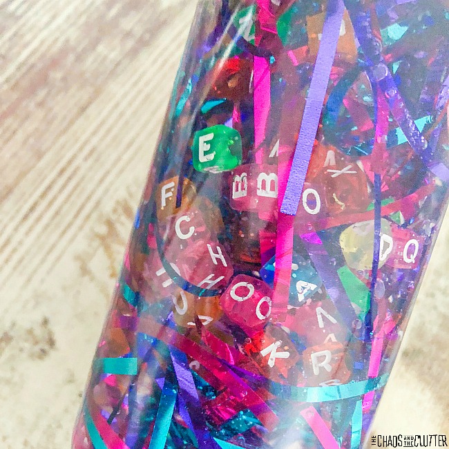A closeup picture of a sensory bottle filled with bright colours of alphabet beads and bright coloured tinsel.