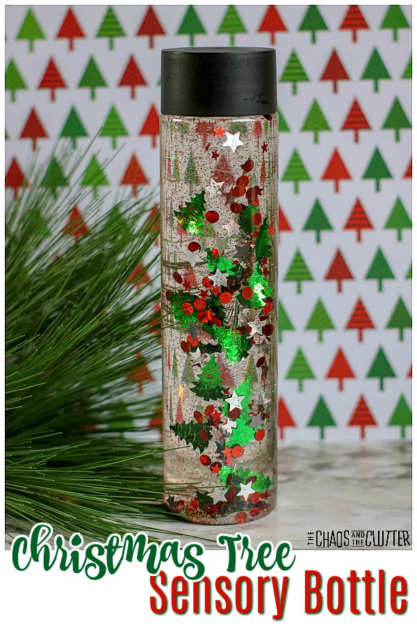 bottle filled with clear liquid and floating red and green tree confetti and glitter with green pine near and text that reads "Christmas Tree Sensory Bottle"