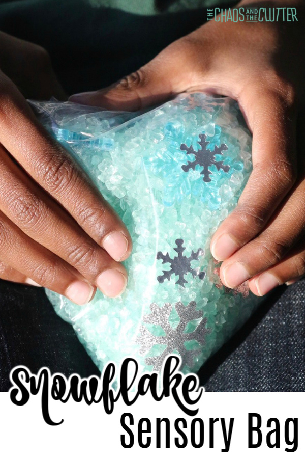 a child's hands holding a bag with blue glitter rocks and silver snowflakes. Text reads "Snowflake Sensory Bag"