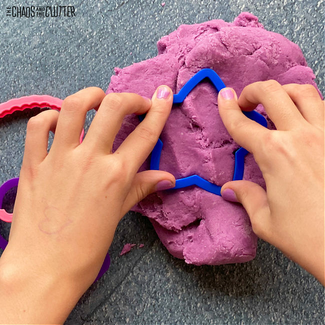 child's hands press a star shaped cookie cutter into purple playdough