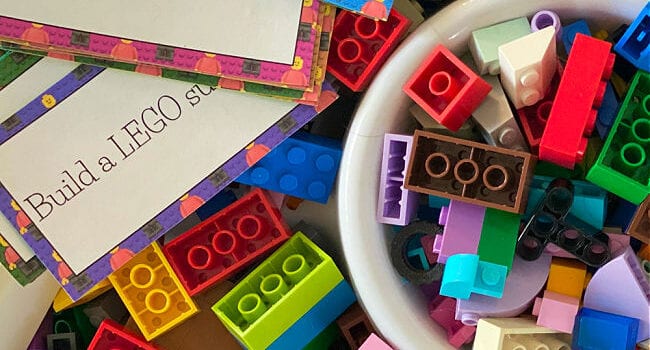 a pile of building blocks with some in a small bowl and printed instruction cards