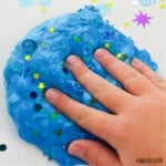 hand presses into blue slime with coloured confetti in it
