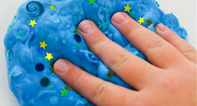 hand presses into blue slime with coloured confetti in it
