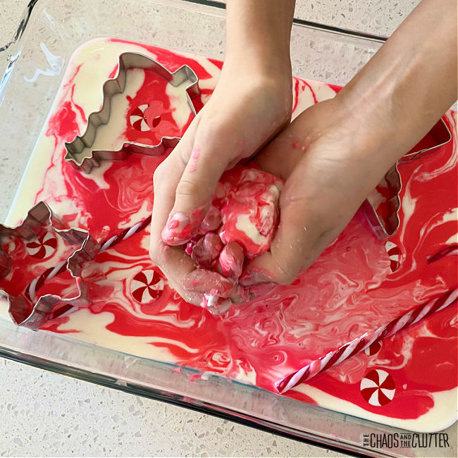 tray of red and white oobleck and candy canes with a pair of hands squeezing the oobleck