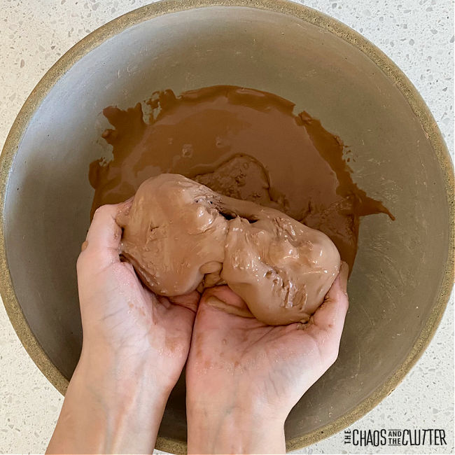 hands hold clumps of a brown material over a bowl