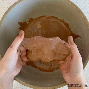a child's hands pull a brown sensory material over a bowl