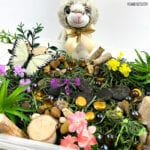 plush bunny sits by a sensory bin filled with moss, grass, and toy butterflies