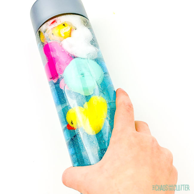 small hand holding a sensory bottle with blue water and rubber ducks in it